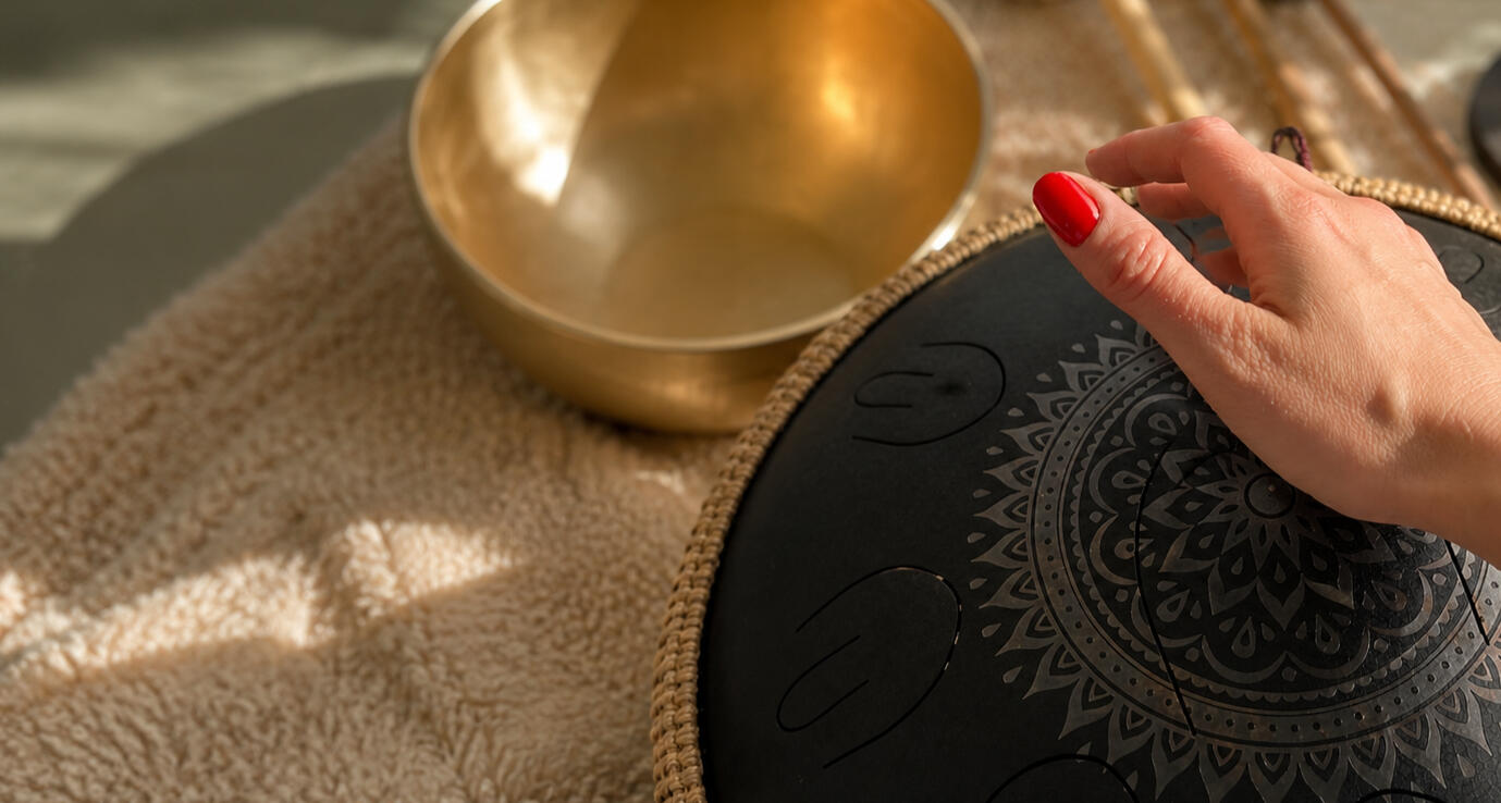Hånd over handpan med klangskål og bløde tekstiler i baggrunden