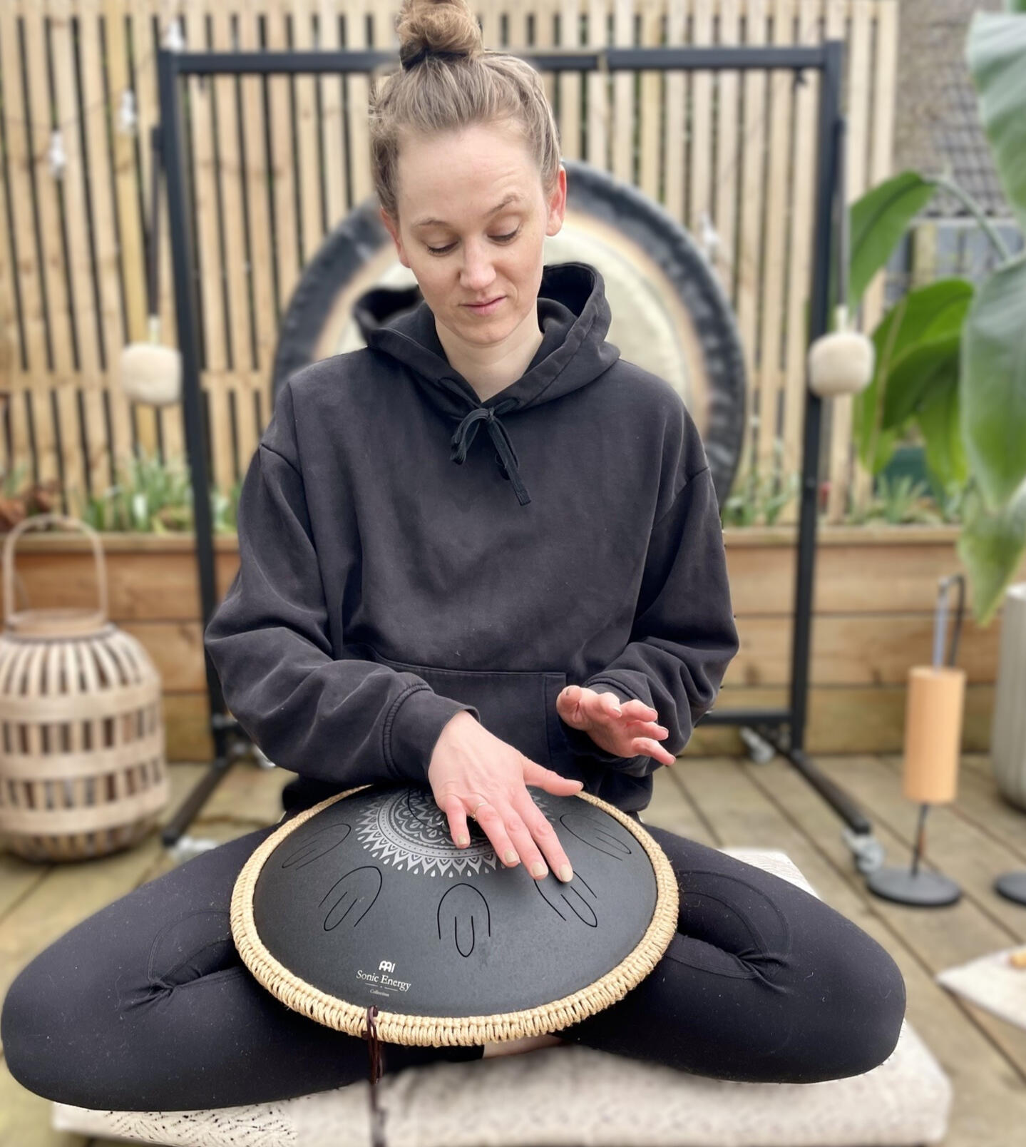Hånd over handpan med klangskål og bløde tekstiler i baggrunden